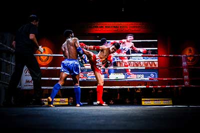 Two Muay Thai fighters exchange kicks inside the ring.