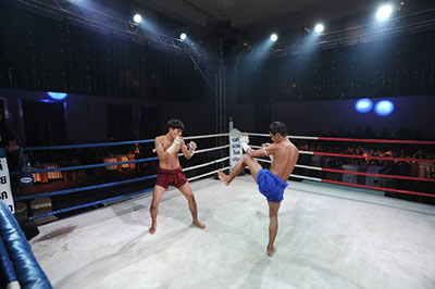 Two Muay Thai fighters square off inside the ring in red and blue shorts.