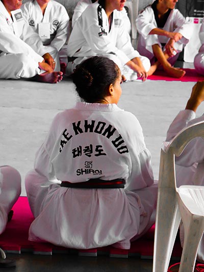 A female taekwondo student sitting on the ground in the dojo.