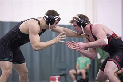 Two amateur collegiate wrestlers wearing their ear protection during a match.