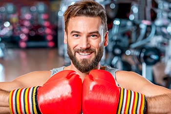 A boxer with a beard in the gym with two red gloves.