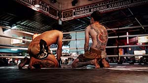 Two pro muay thai fighters kneel in the ring.