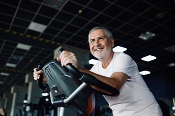 A smiling elderly man on a cycling machine in the gym.
