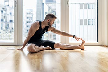 A sole man does yoga leg stretch beside window.