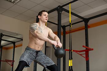 A man doing kettlebell swings in the gym.