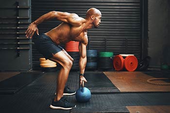 A man uses a blue kettlebell in the gym.